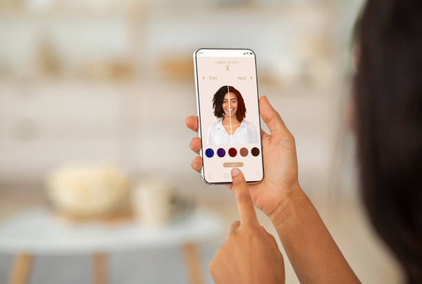 携帯電話で髪の色シミュレーション アプリを使用する女性の肩越しに、拡張現実システムを備えた現代美容アプリケーションでさまざまなヘアスタイルを試して、創造的なコラージュ、クローズ アップ