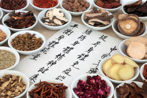 Výběr tradičních čínských léčivých bylin v porcelánových miskách s kaligrafickým písmem na rýžovém papíře.Překlad popisuje čínskou bylinnou medicínu jako zvyšující schopnost těla udržovat zdraví těla a ducha a vyrovnávat energii.