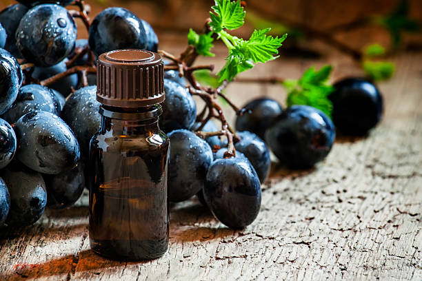 Minyak wiji anggur ing botol coklat, sekelompok anggur, anggur ing latar mburi kayu lawas, fokus selektif