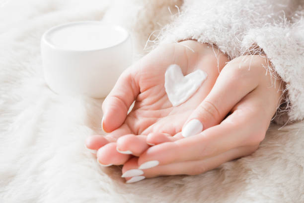 푹신한 담요 위에 크림병을 얹은 아름다운 손질된 여성의 손.겨울철 깨끗하고 부드러운 피부를 위한 수분 크림.크림으로 만든 하트 모양.몸을 사랑하세요.건강 관리 개념입니다.