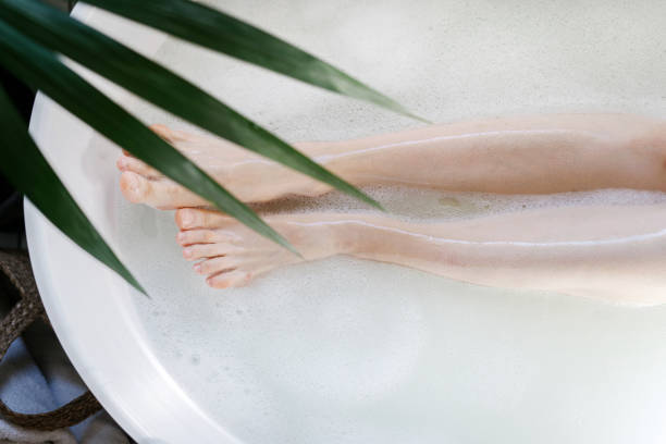 Cropped shot of female legs. Top view of woman lying in bathroom tub with warm water and bubbles. Epilation, depilation, skin care concept. Girl take bath in tropical hotel, enjoy beauty spa procedure
