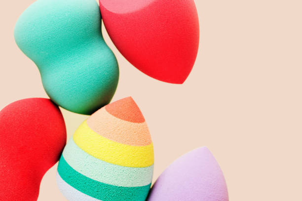 Colored cosmetic beauty blender sponges on nude colored background with copy space. Green, violet, pink, rainbow colored sponges different shape.