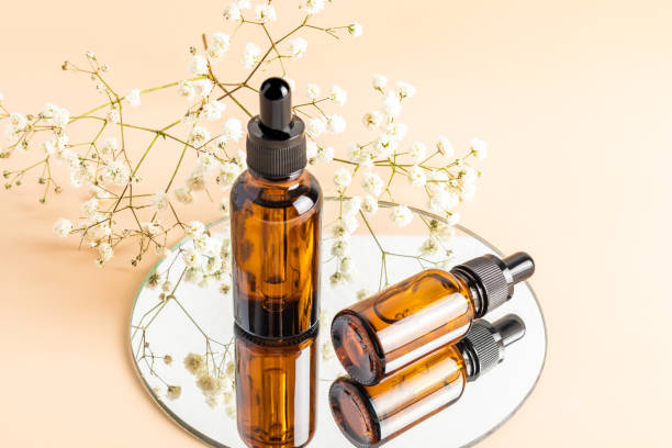 two glass bottles with a dropper for facial skin care on a round mirror with white gypsophila. natural cosmetics. moisturizing. beige background